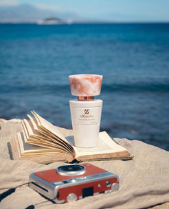 Flacon blanc Olfazeta by Chogan Millésime N°29, bouchon marbré rose, sur un livre ouvert face à la mer
