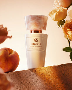 Flacon blanc Olfazeta by Chogan Millésime N°27 sur pierre avec une pêche et des roses pêche, lumière dorée