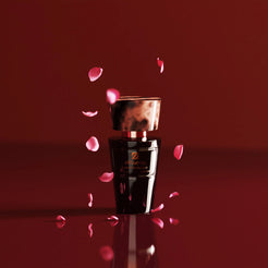 Flacon noir Olfazeta by Chogan Millésime N°162 à capuchon marbré sous une pluie de pétales de rose sur fond bordeaux